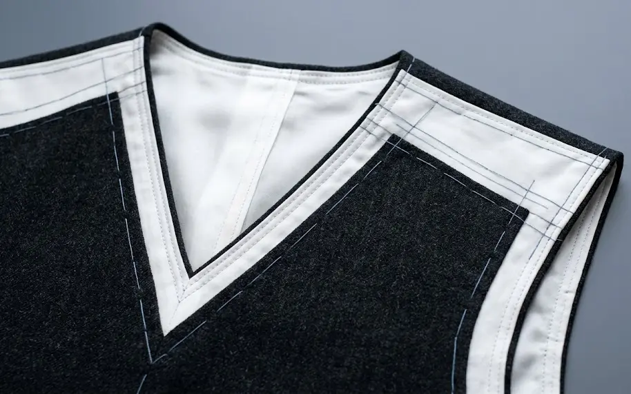 Detalle lineal y limpio de los cortes y costuras de un cuello en V iluminado frontalmente en un vestidor premium.